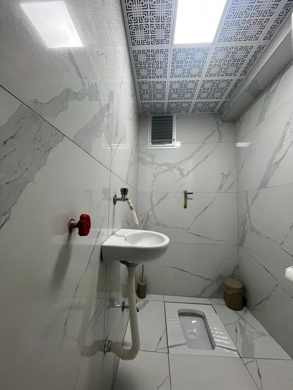 Mermer desenli duvar seramikleri, lavabo ve alaturka tuvalet bulunan alan